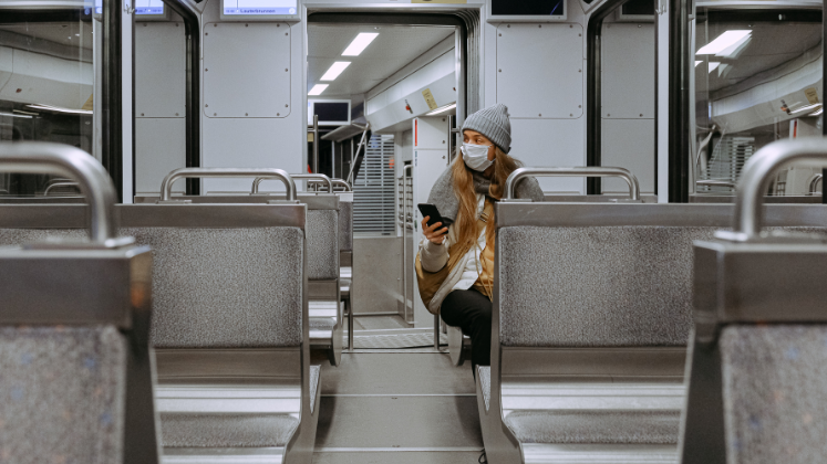 Woman on empty train wearing face mask_sourced via Canva_747x420