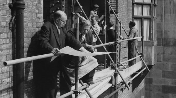 Work on LSE courtyard extension in 1964, two men look at plans while builders in the background work