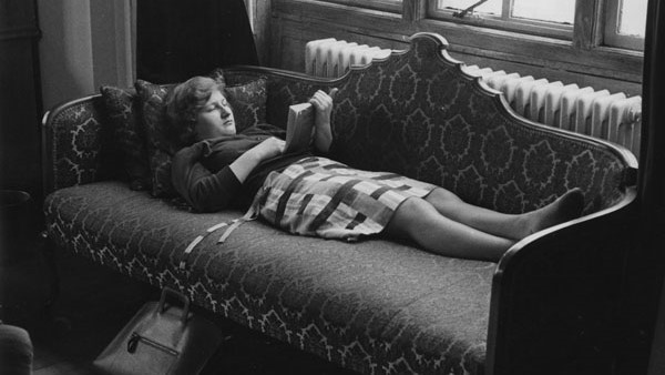 Student reading a book lying on a sofa in the Shaw Library in 1964