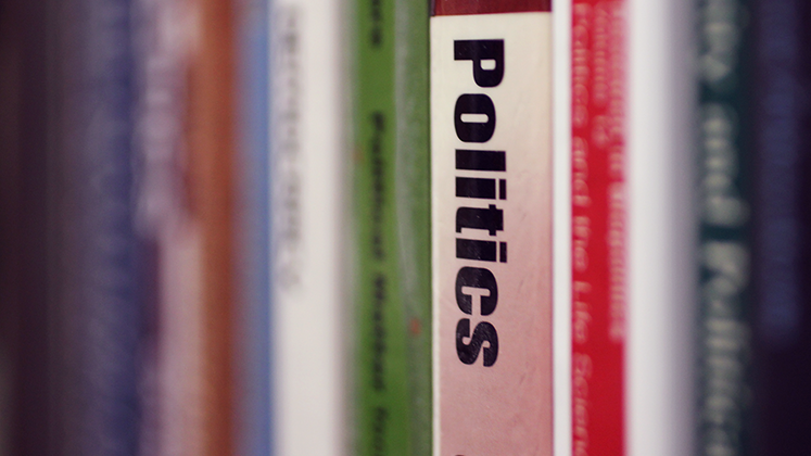 Abstract image of books on a library shelf, with the word 'politics' on the spine of a book in sharp focus whilst everything else is blurred.