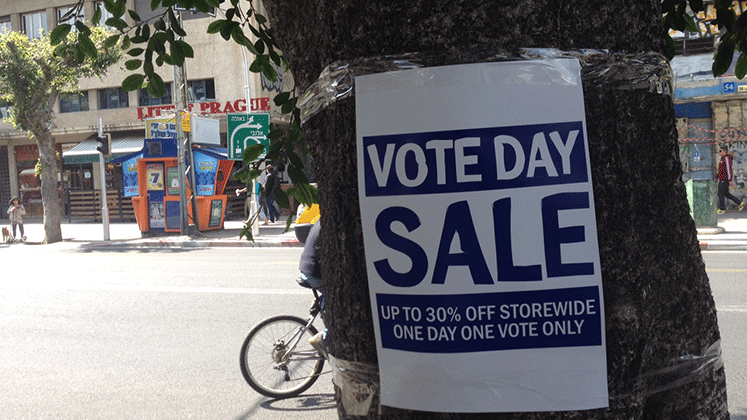 Sign stapled to a tree about a voting day sale for a shop