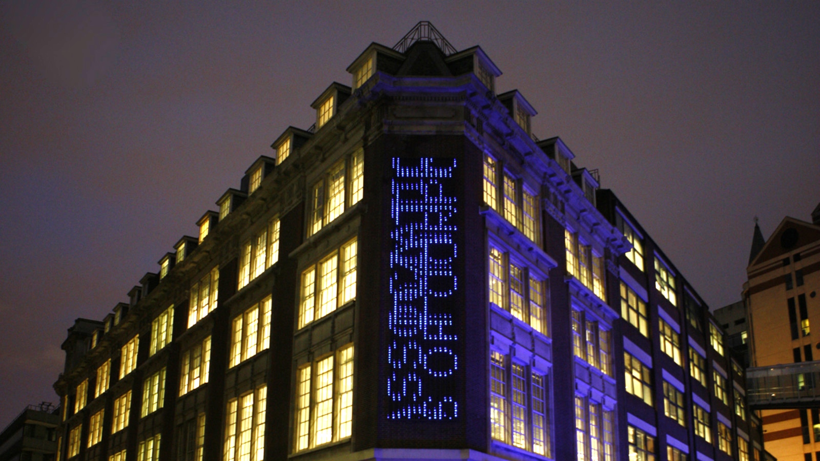 A view of LSE Library from outside at night with a focus on the Bluerain artwork on the corner of the building.