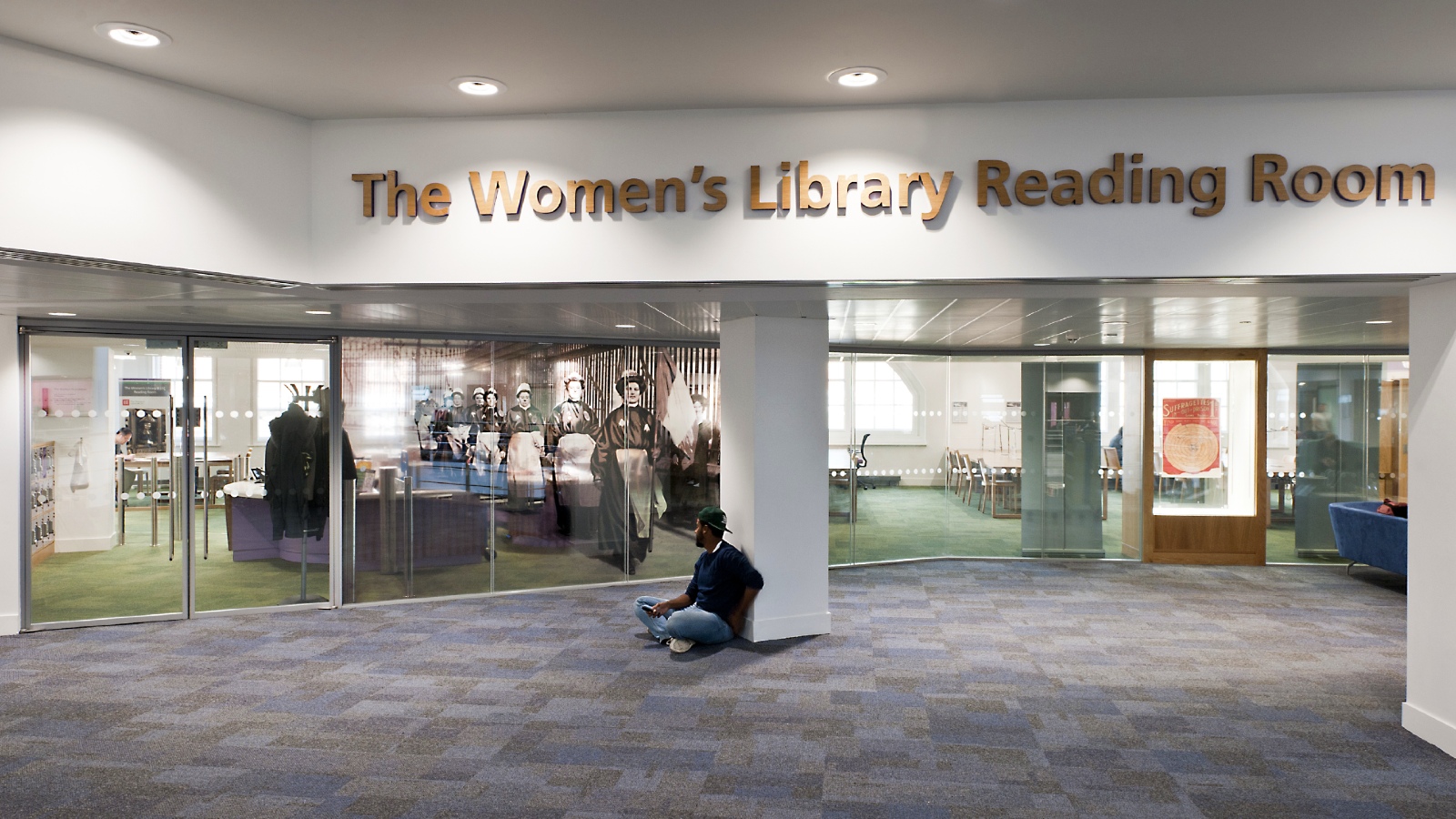A view on the 4th floor of the Library outside and looking into The Women's Library Reading Room. A student is seated on the floor.
