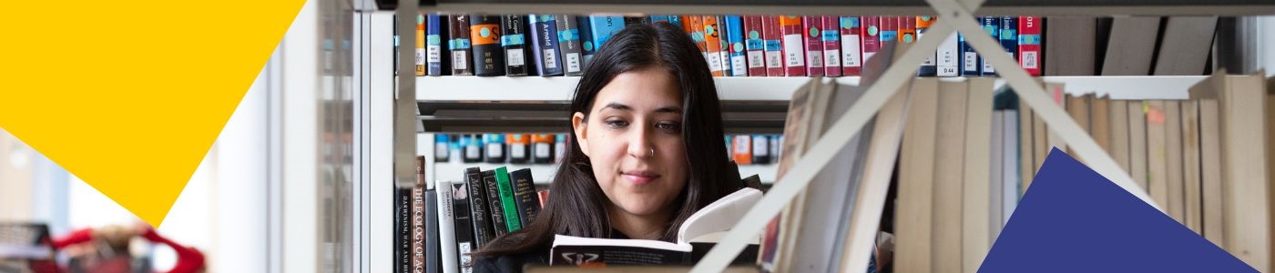 A student reading a book in the stacks