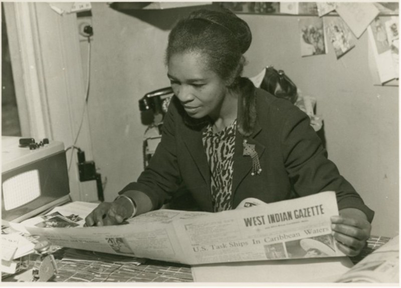 A woman sat at a desk reading a newspaper