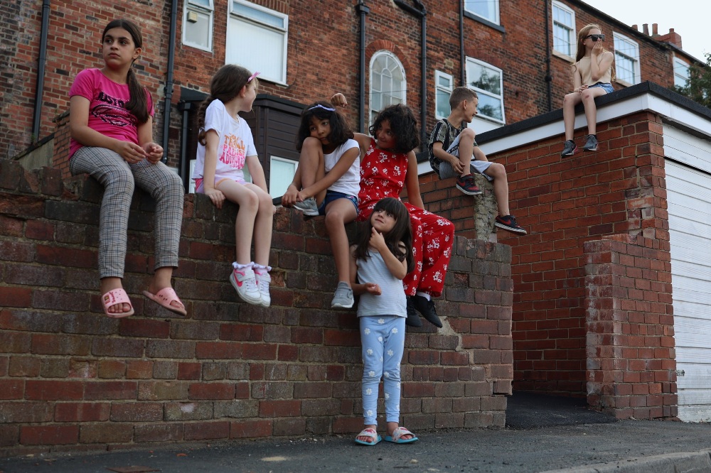 A group of children on a street mostly sat on a brick wall