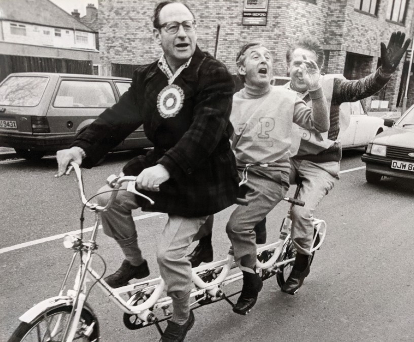 Three men on a bike waving