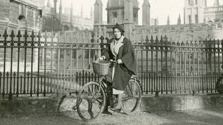 A woman wearing academic dress on a bicycle in Oxford