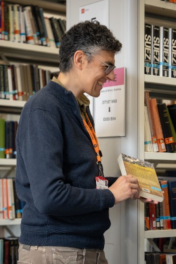 A smiling member of staff holding a book while in the stacks.