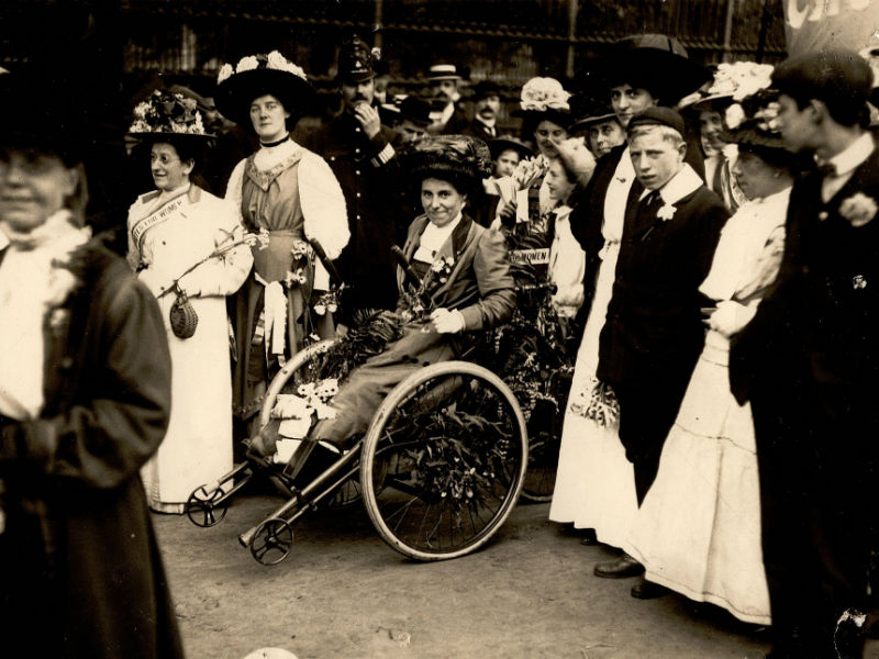 Rosa May Billinghurst sitting in her tricycle surrounded by people