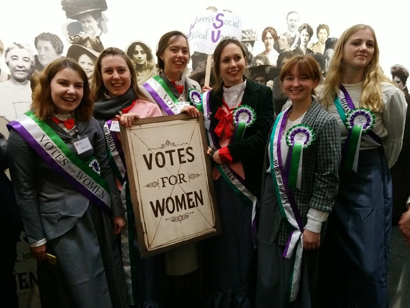 a group of people dressed as suffragettes holding a banner