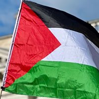 A Palestinian flag in front of a building with blue skies above.